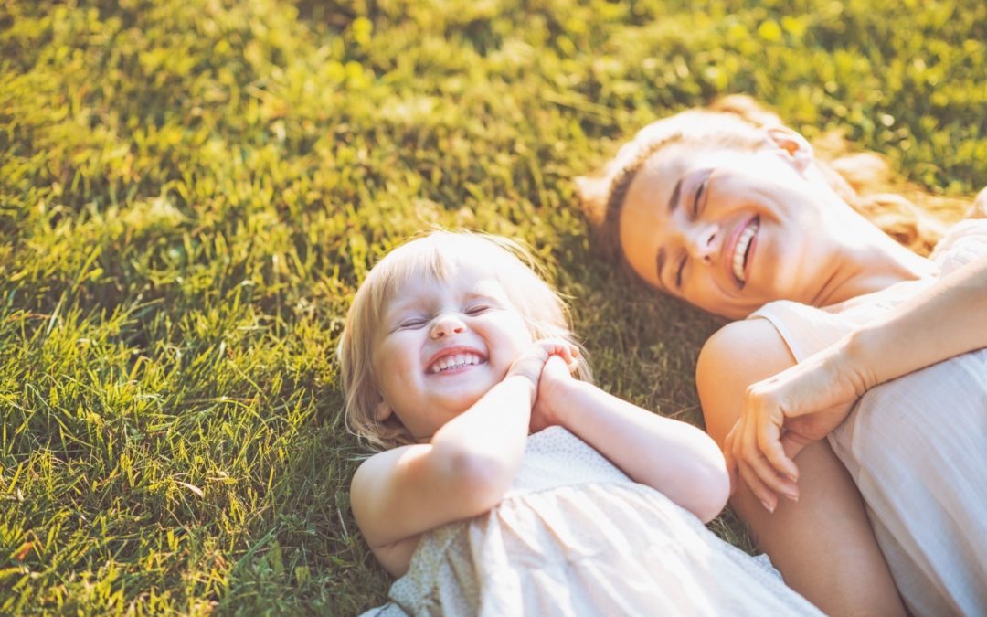 A mom and daughter laying down in the grass with big smiles on their faces